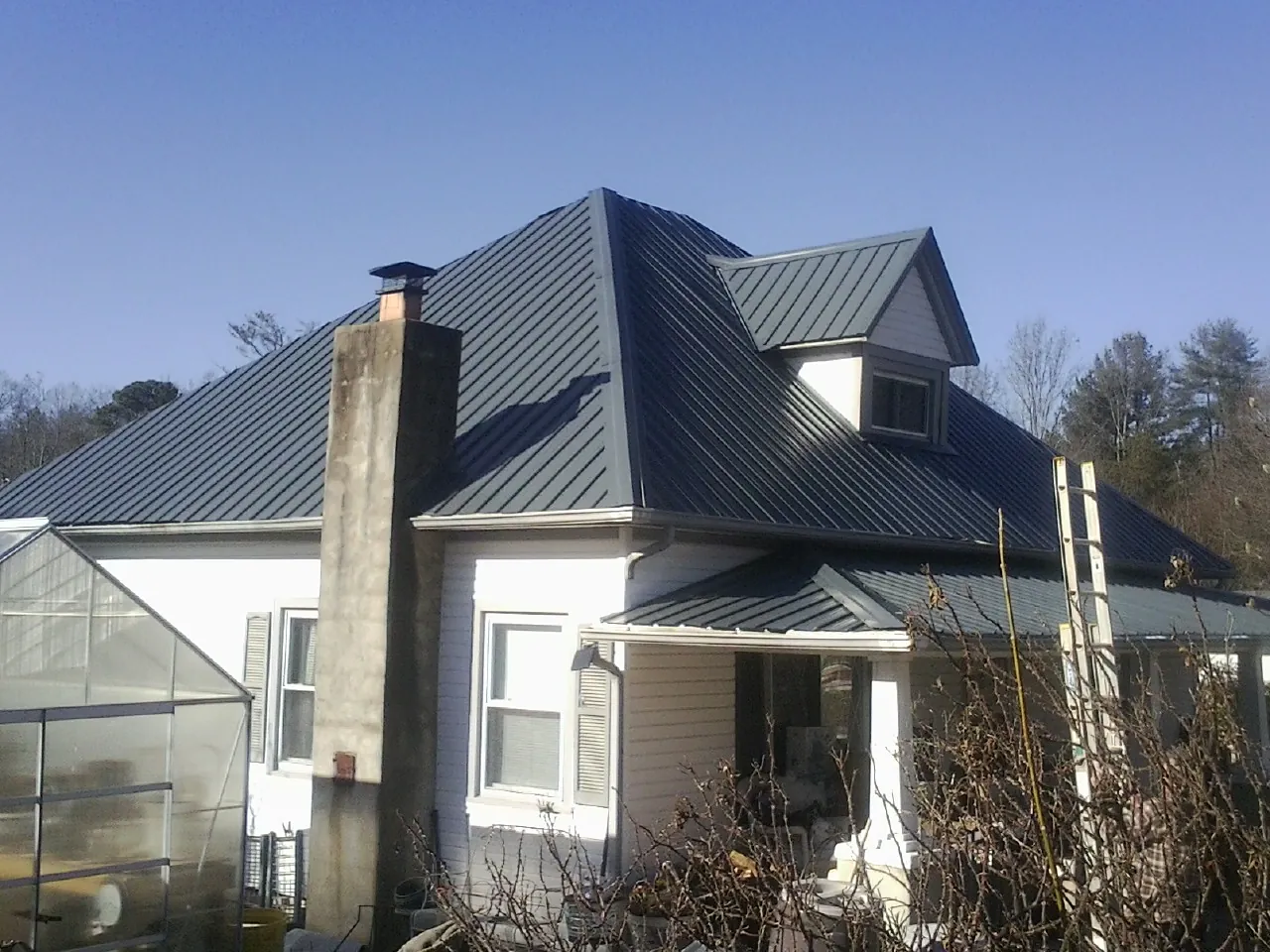 Dark blue standing seam metal roof on a white farmhouse with dormer — Slate & Tile Roof Repair by Roofing Brothers in Cimarron