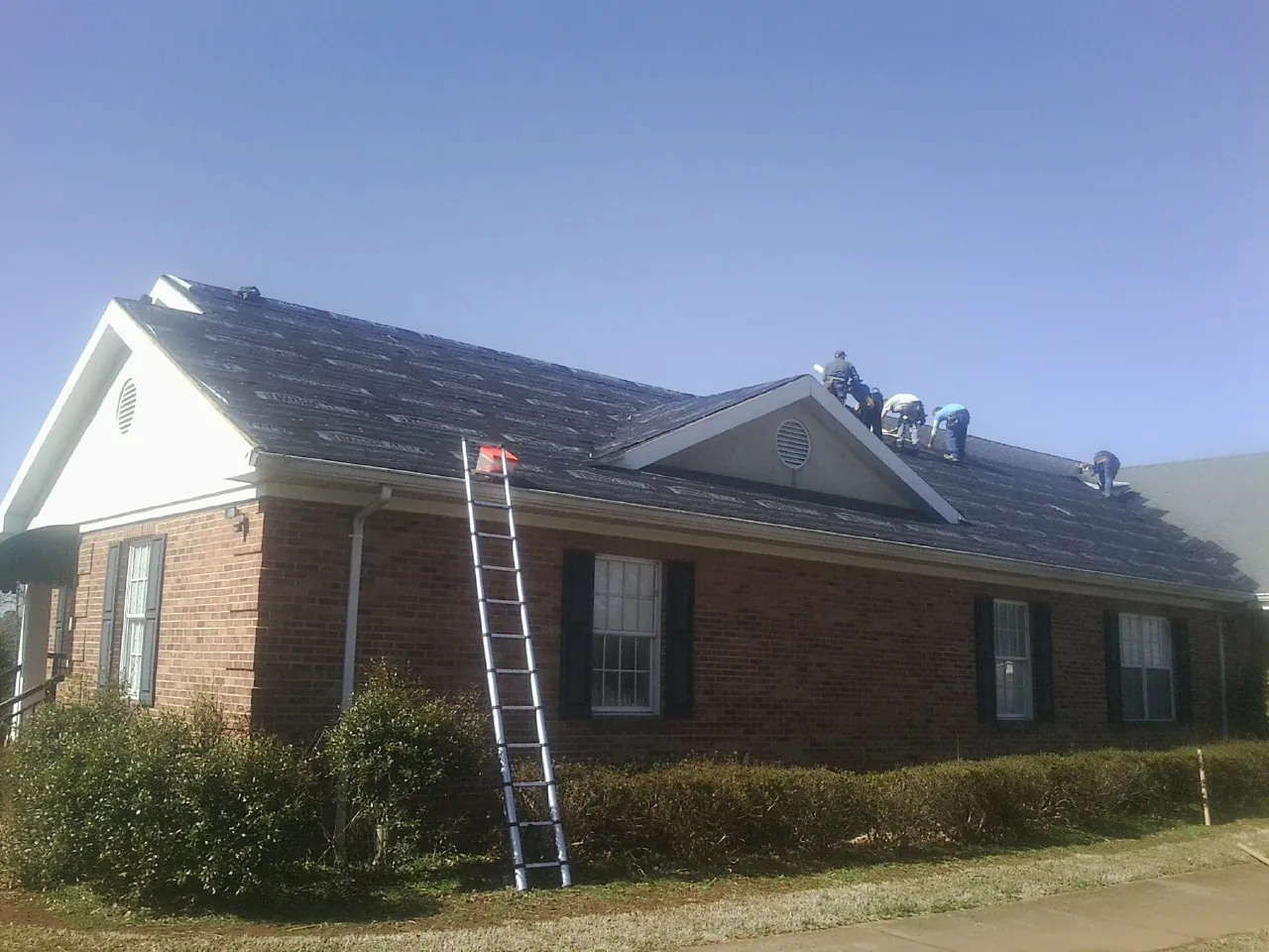 Crew tearing shingles off a brick ranch roof with a ladder set — Emergency Roof Repair work by our crew in Cimarron