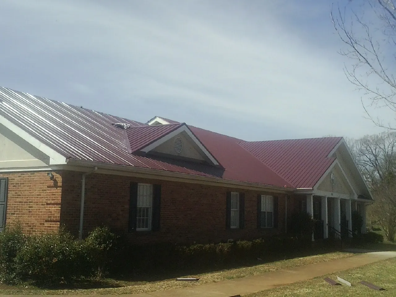 Red metal roof with gabled entries on a long brick building, from a Hail Damage Roof Repair job in Cimarron