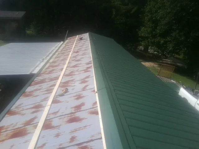 Old rusted panels beside newly installed green metal roofing — Wind Damage Roof Repair by Roofing Brothers in Cimarron