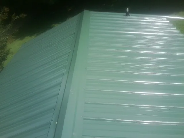 New green metal panels meeting at the ridge of a roof — Flat Roof Repair work by our crew in Cimarron