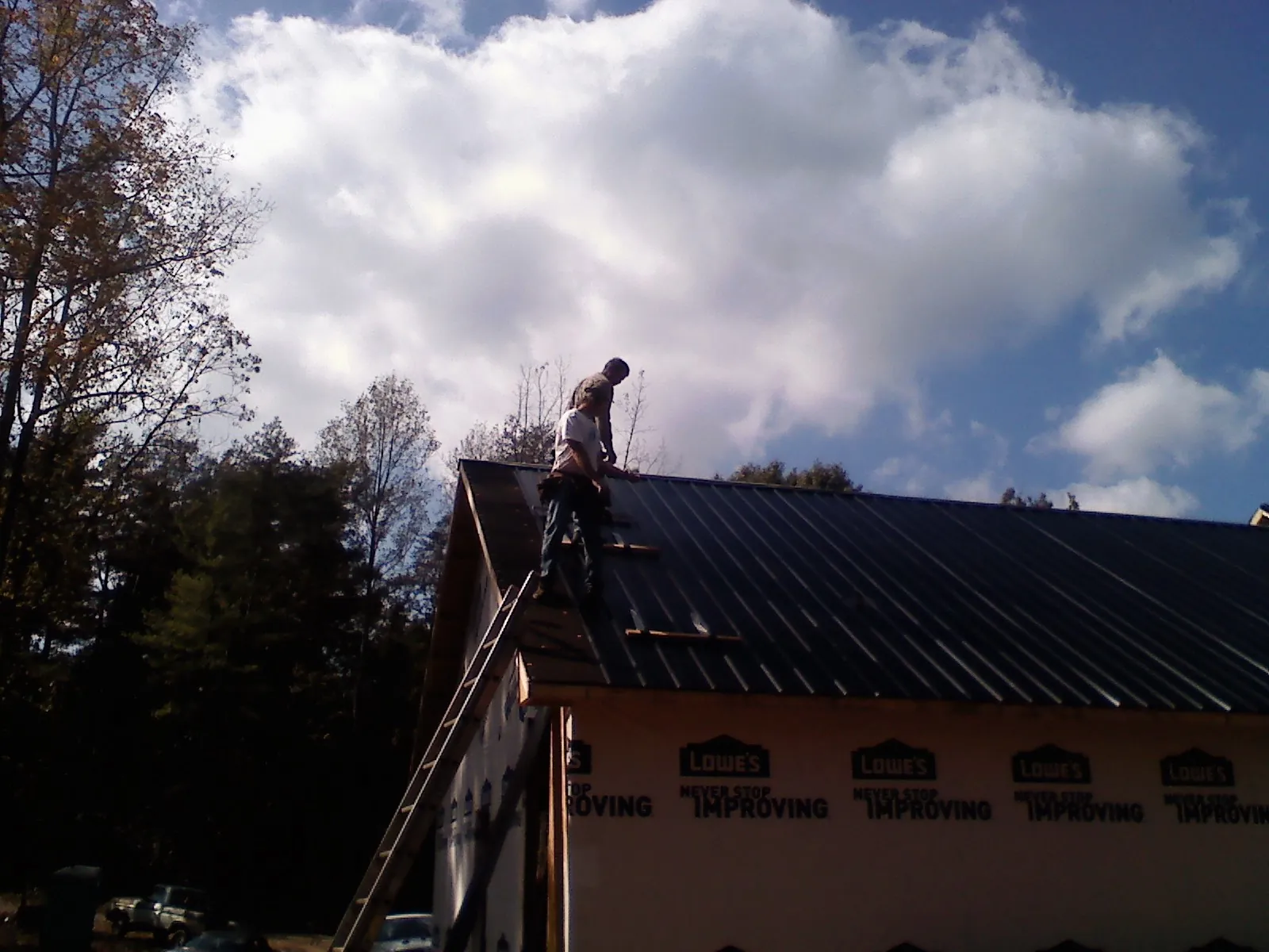 Roofer fastening dark metal panels high against a cloudy sky, from a Roof Inspection job in Cimarron