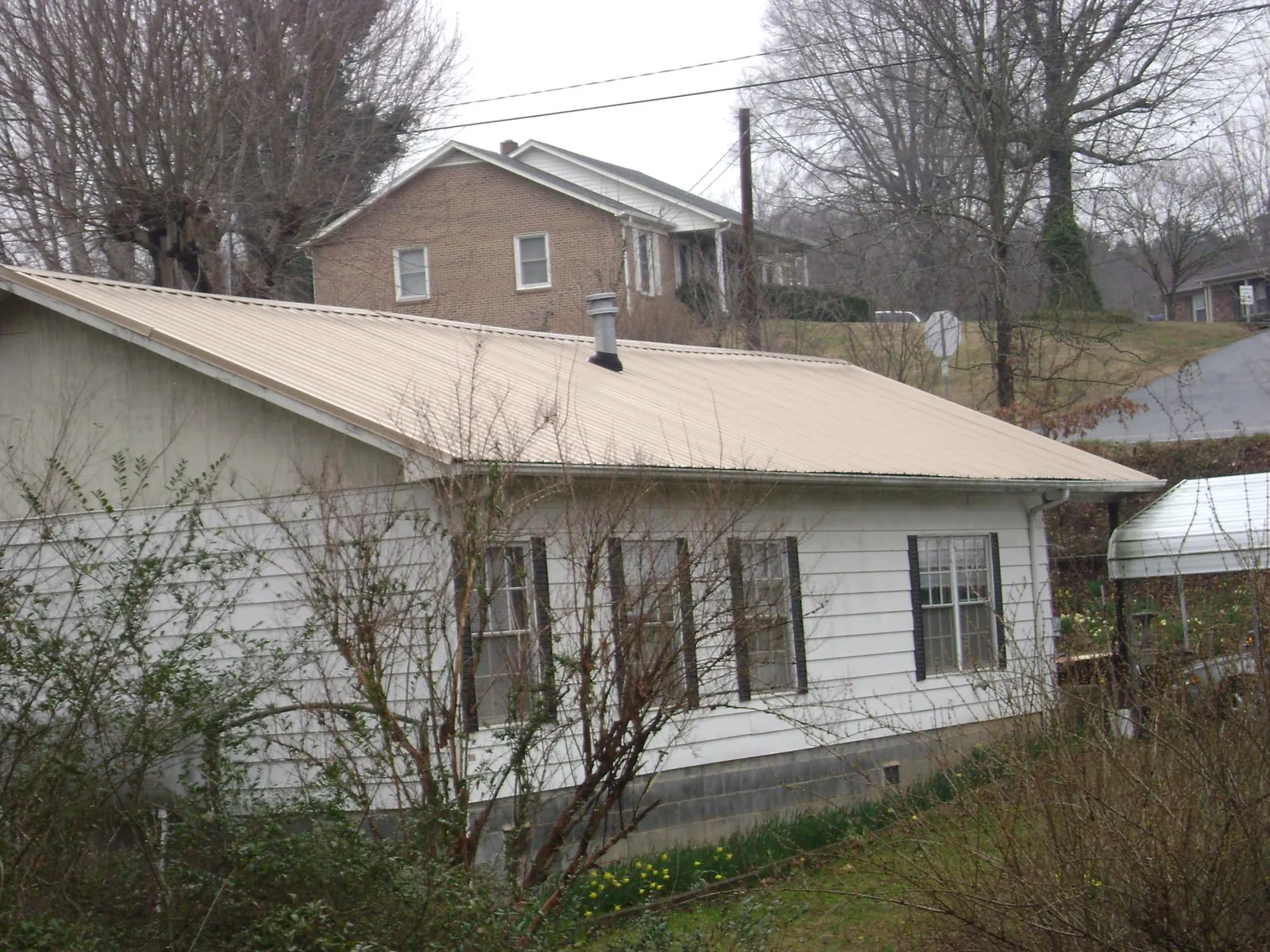 Tan metal roof on a white sided house set into a hillside — Commercial Roofing by Roofing Brothers in Cimarron